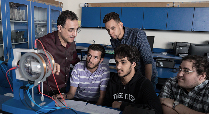 أربعة من طلبة درجة البكالوريوس في الهندسة الكهربائية في جامعة أبوظبي يناقشون مشروع دراسي مع أستاذهم